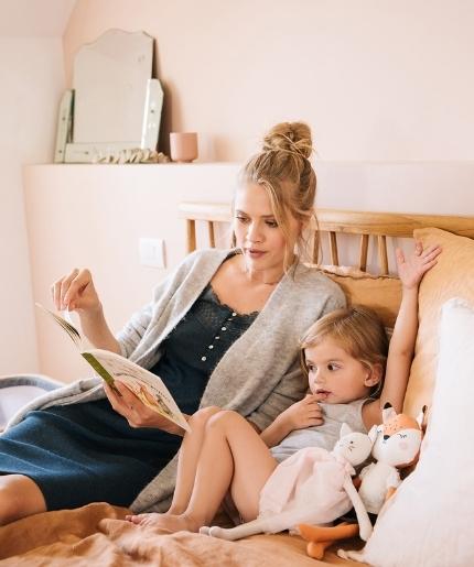 Mutter liest Tochter entspannt im Bett ein Buch vor